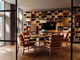 A modern library with a large bookshelf, a flat-screen TV, and leather chairs around a wooden table.
