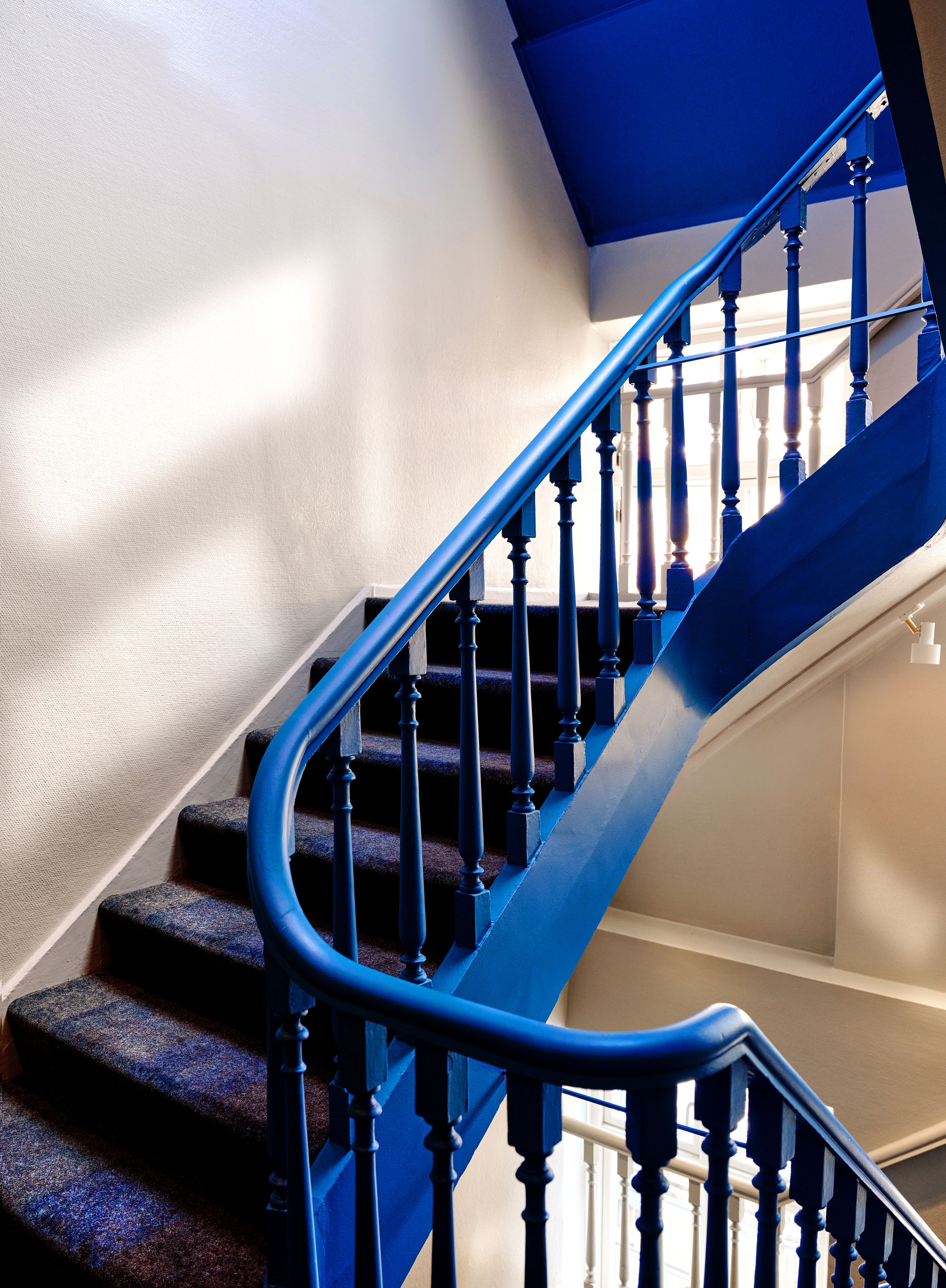 Un escalier en colimaçon avec des rampes bleues et des balustres en bois, menant à l’étage supérieur.