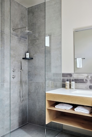 Un baño moderno con ducha de vidrio, tocador de madera y lavamanos blanco, además de un espejo sobre el lavamanos.