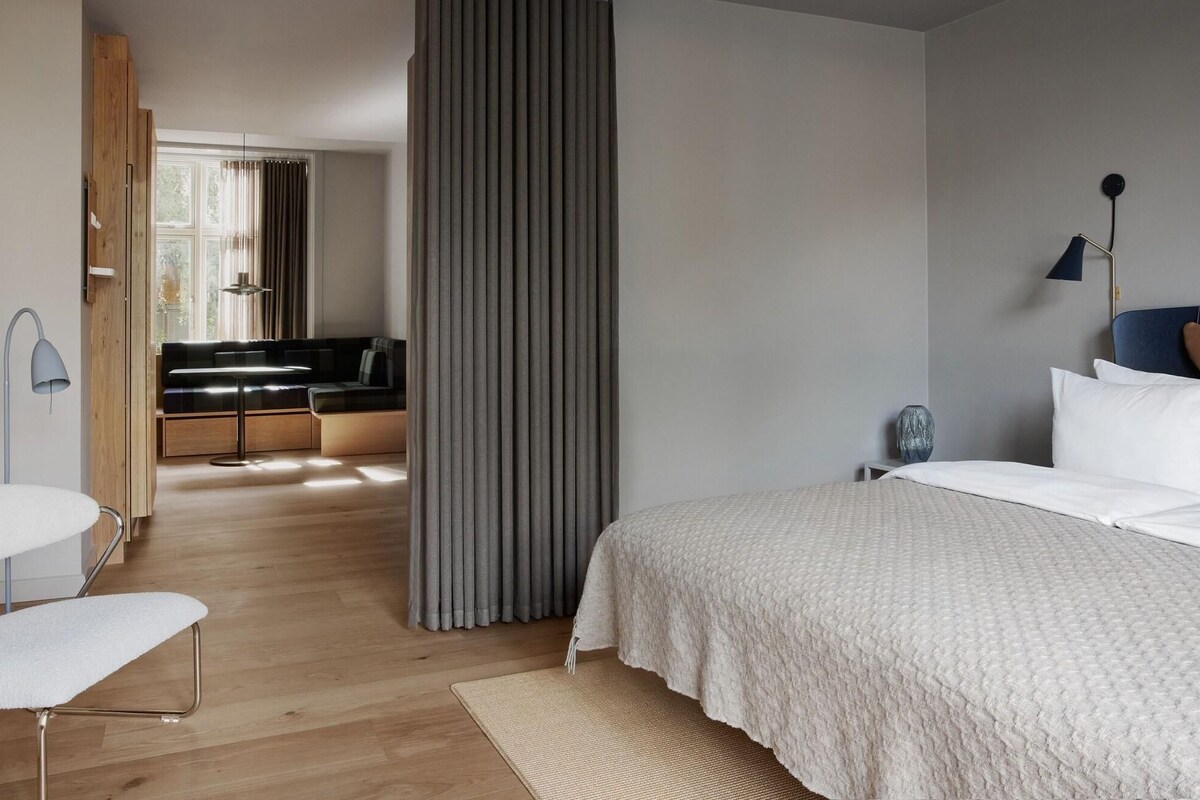 Une chambre moderne comprenant un lit, une table de chevet, une lampe et un coin salon avec un canapé et des rideaux.