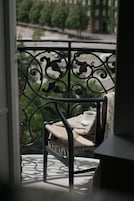 A balcony with a wrought iron railing, a chair with a cushion, and a table with a cup of coffee.