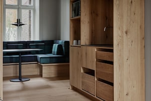 A modern kitchen with wooden cabinetry, a built-in bench with cushions, and a round table.