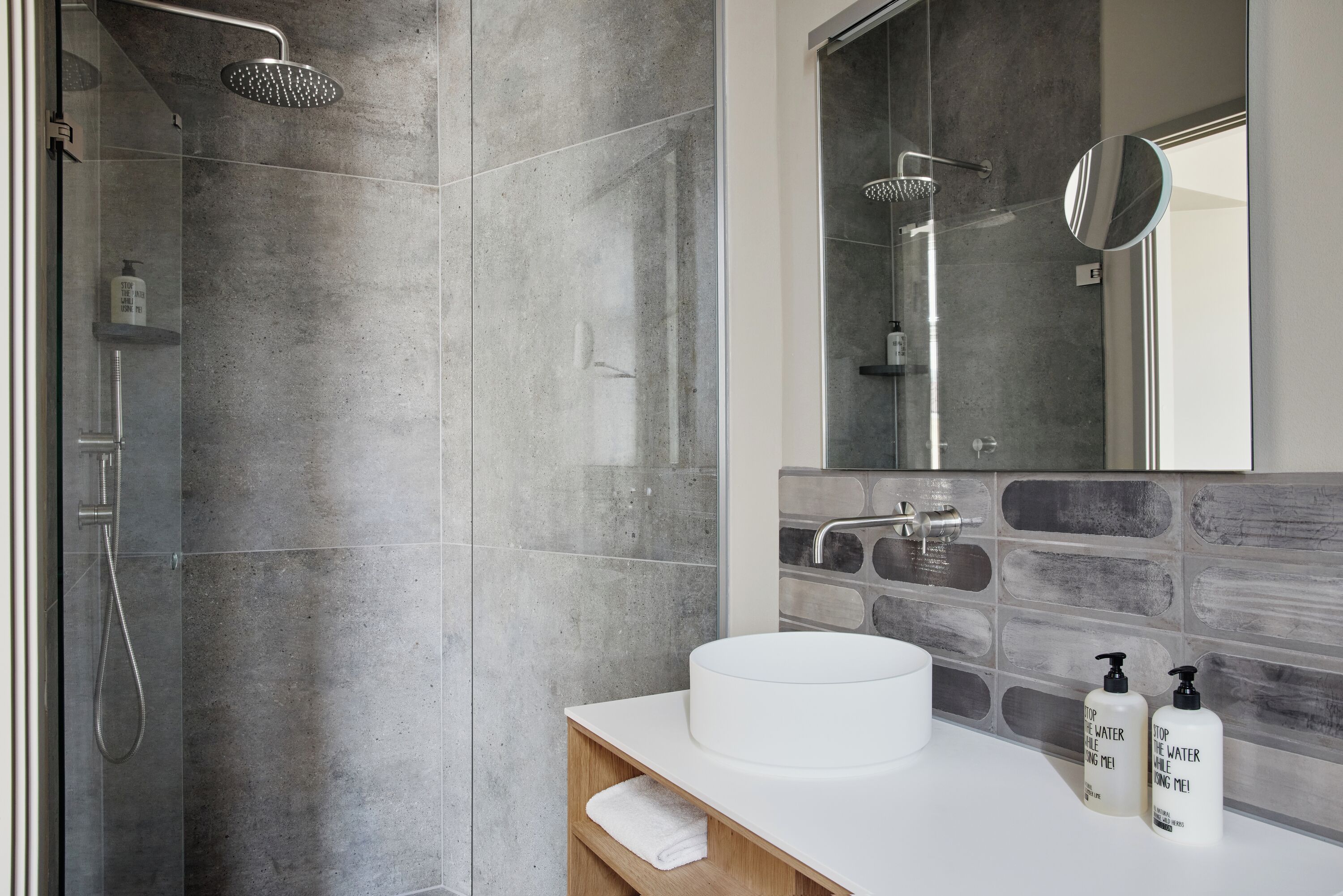 A modern bathroom with a glass-enclosed shower, a white sink, and a mirror above it.