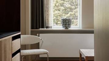A room with a large arched window, a wooden floor, a white chair, a small round table, and a wall-mounted lamp.