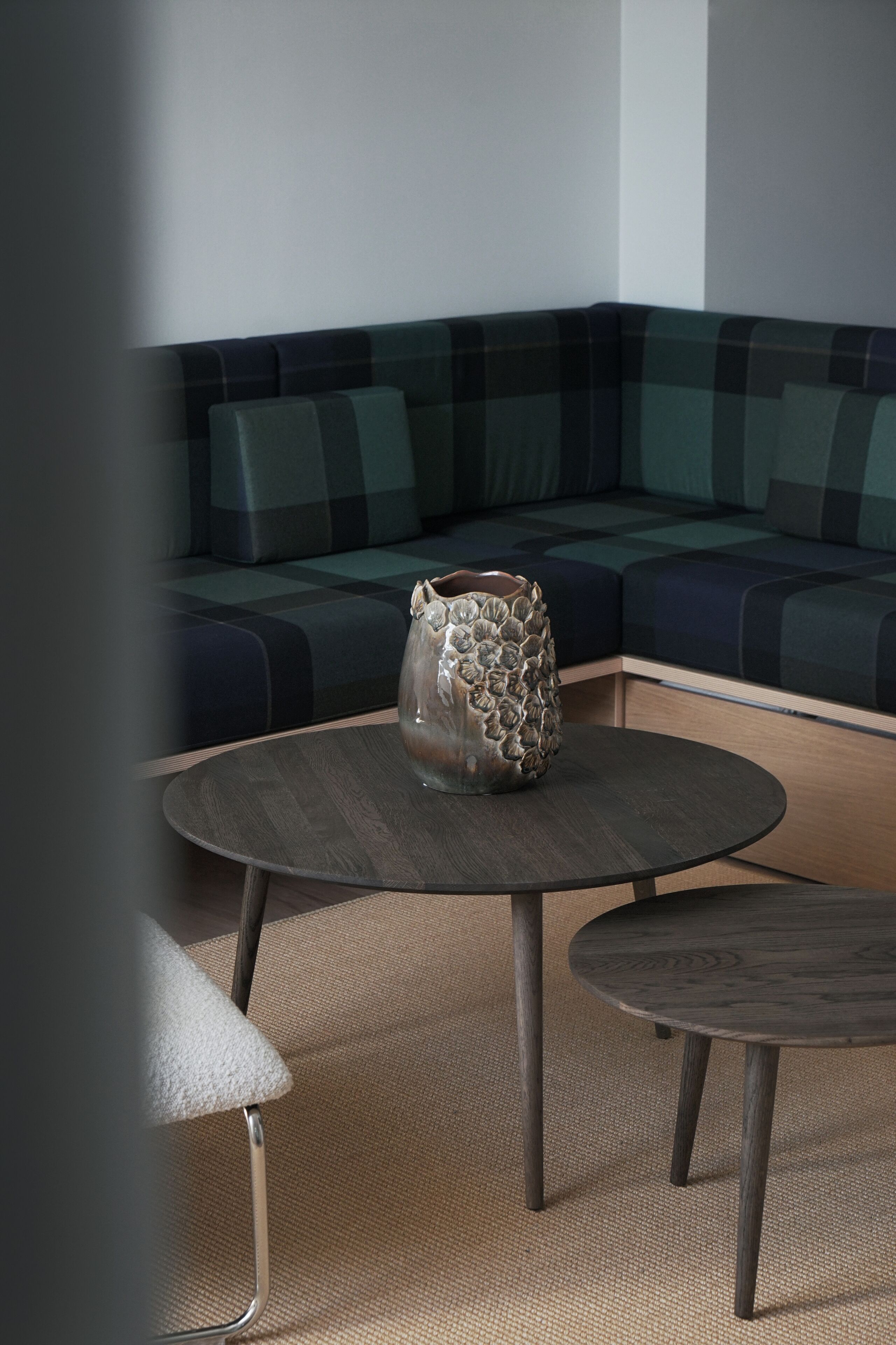 A modern living room with a round wooden table, a glass vase, and a sofa with a checkered pattern.