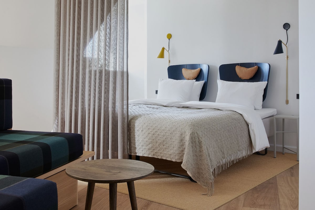 Un dormitorio moderno con una cama, mesitas de noche, una mesa redonda y un cortinero divisorio.