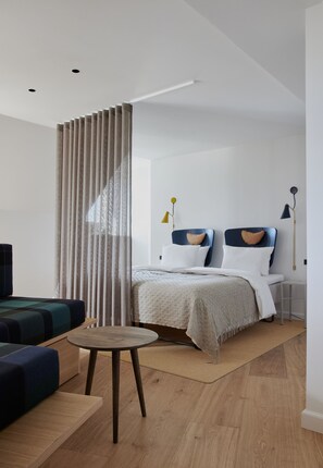Un dormitorio moderno con una cama, mesitas de noche, una mesa redonda y un cortinero divisorio.