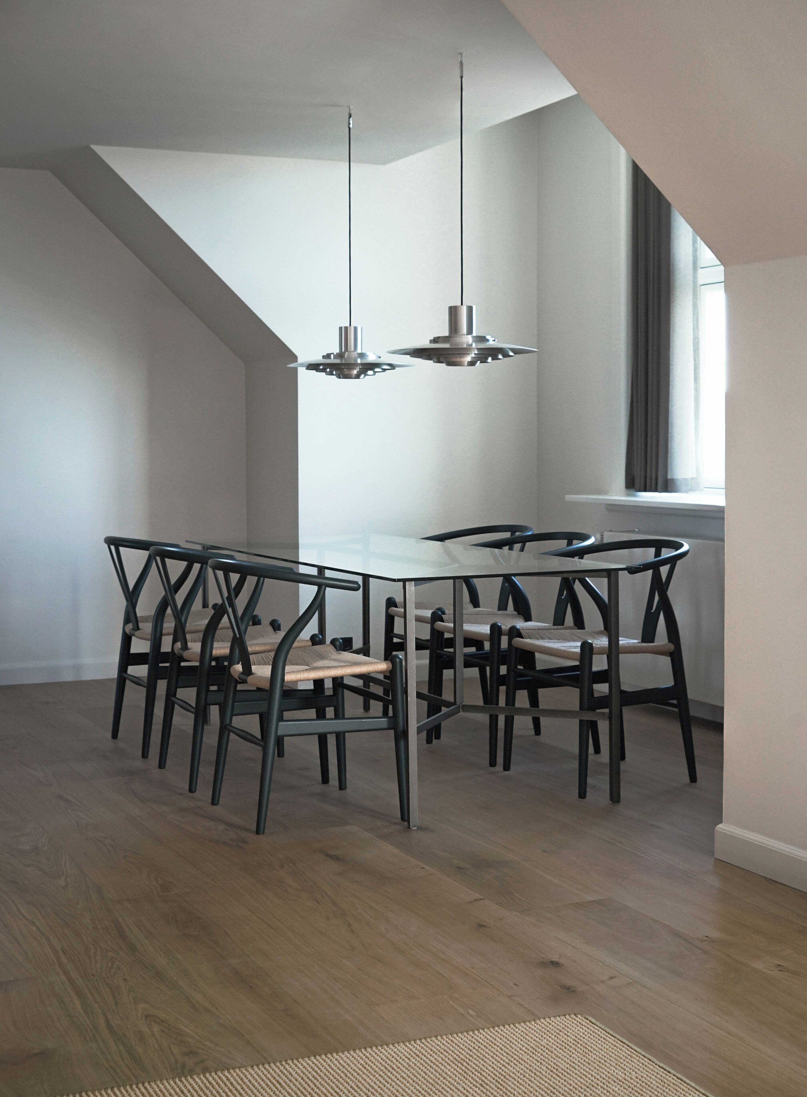 A dining area with a white table and black chairs, wooden flooring, and pendant lights.