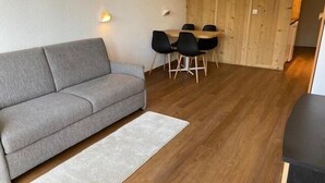 Ein modernes Wohnzimmer mit einem grauen Sofa, einem Holzesstisch mit Stühlen und einem hellen Teppich.