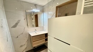 Ein modernes Badezimmer mit Marmorwänden, einem weißen Waschbecken und einem Holzbadezimmerunterschrank.