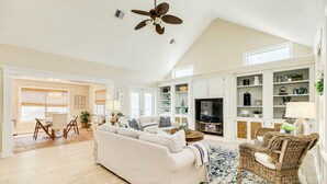 A spacious living room with a high ceiling, a large sofa, a wicker chair, and a television. - Private Canal Home w/ Boat Dock, 2 Living Areas - Fish from the Deck! (Galveston)
