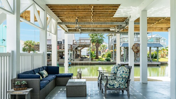 A covered outdoor area with a wicker sofa, a floral chair, and a small table. - Private Canal Home w/ Boat Dock, 2 Living Areas - Fish from the Deck! (Galveston)