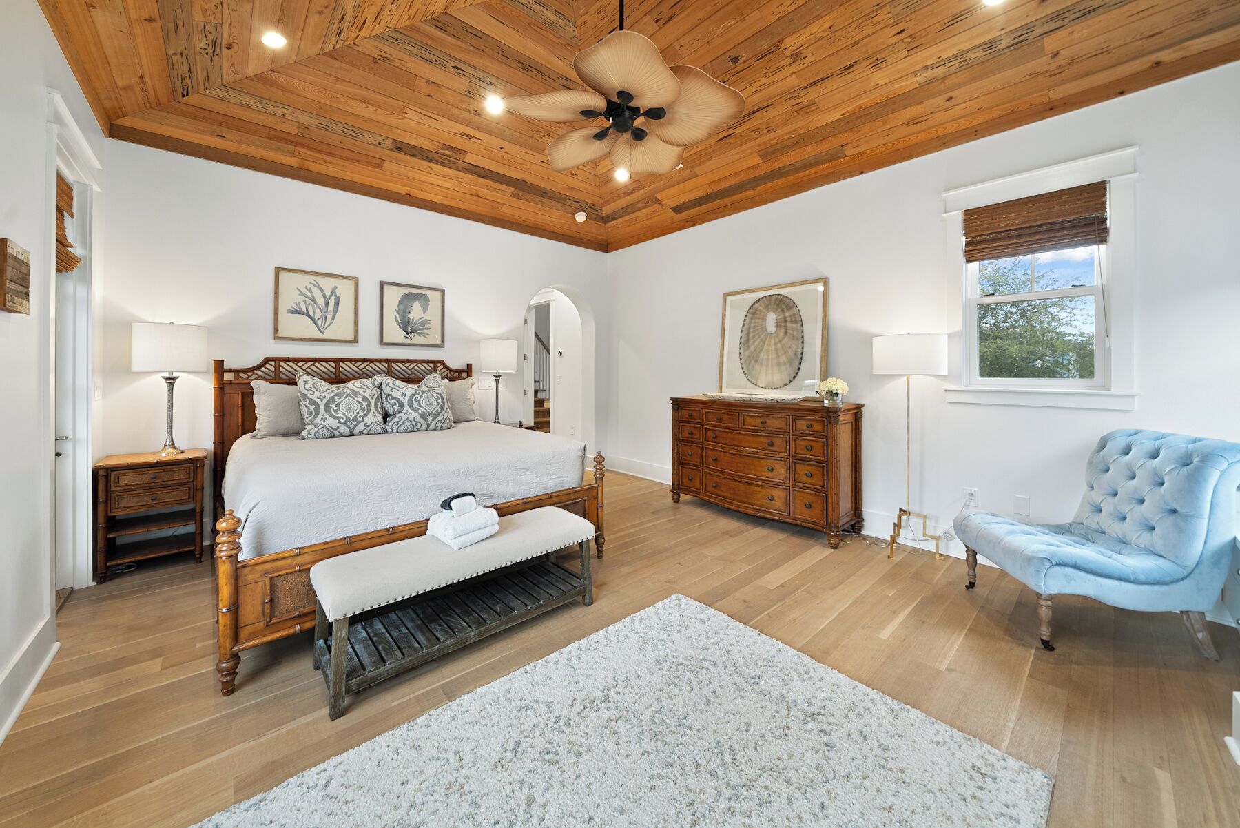 Une chambre avec un plafond en bois, un lit avec une banquette, une commode, une chaise et des œuvres d’art accrochées aux murs.