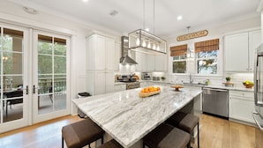 A modern kitchen with white cabinets, a marble island, and a sign reading "BEACH HOUSE". - All Decked Out (Santa Rosa Beach)