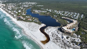An aerial view of a coastal area with a beach, a river, and a residential area with buildings. - All Decked Out (Santa Rosa Beach)