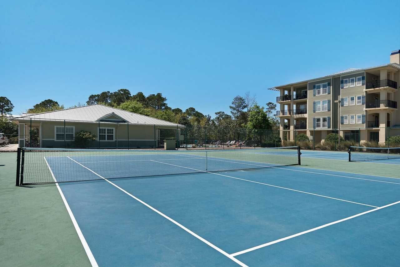 An outdoor tennis court with a net, surrounded by buildings and trees.