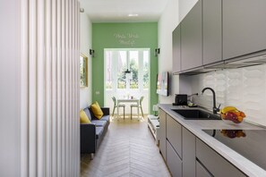A modern kitchen with a herringbone floor pattern, a dining area with a white table and chairs, and a green accent wall with a window. - PortaVerde Miniloft - [3 km form Duomo] (Milano)
