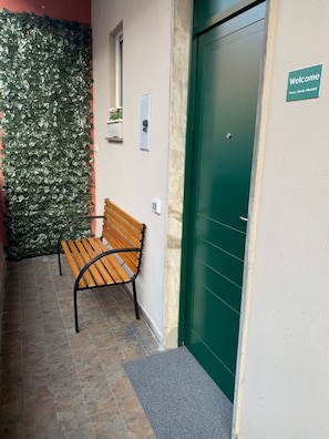 Un banco frente a un edificio con puerta verde y un letrero de bienvenida.