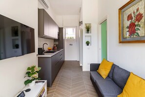 Una cucina moderna con forno integrato e zona pranzo con divano grigio e cuscini gialli.