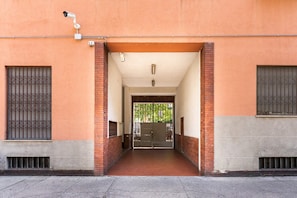 L'ingresso di un edificio con un arco in mattoni, una telecamera di sicurezza e un cancello in metallo.