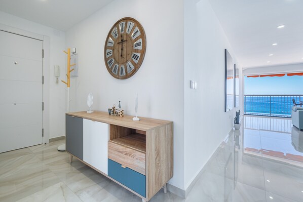 Une chambre d’hôtel moderne avec une horloge en bois, une armoire en bois et bleue, et un balcon avec vue sur la mer.