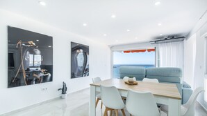 Ein modernes Wohnzimmer mit Esstisch, weißen Stühlen, einem blauen Sofa und einem großen Fernseher an der Wand.
