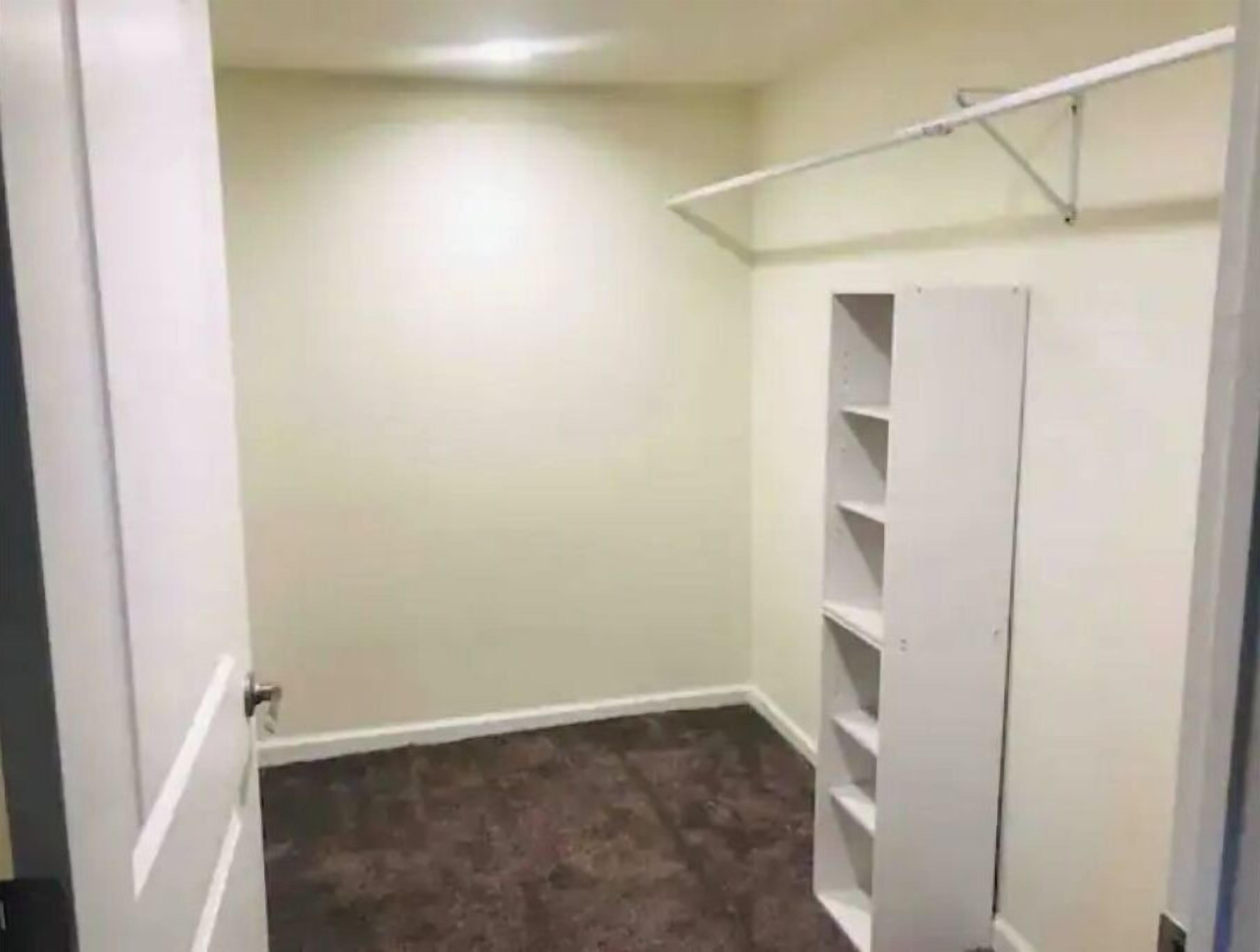 Un placard avec des étagères blanches et une tringle en métal pour suspendre les vêtements.