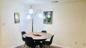 A dining area with a round table, black chairs, and a floor lamp. There are two framed pictures on the walls.