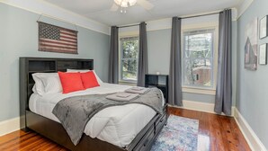 Une chambre à coucher avec un lit, un ventilateur de plafond, une fenêtre avec des rideaux et un drapeau américain accroché au mur.
