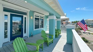 A blue house with a porch, green Adirondack chairs, and an American flag. - Drift Away Shores · Steps to the beach!*Week Discount*Tiki Bar*2 Pools (Gulf Shores)