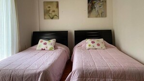 Dos camas individuales con cabeceras a juego y almohadas estampadas con motivos florales, un cuadro en la pared y una ventana con cortinas.