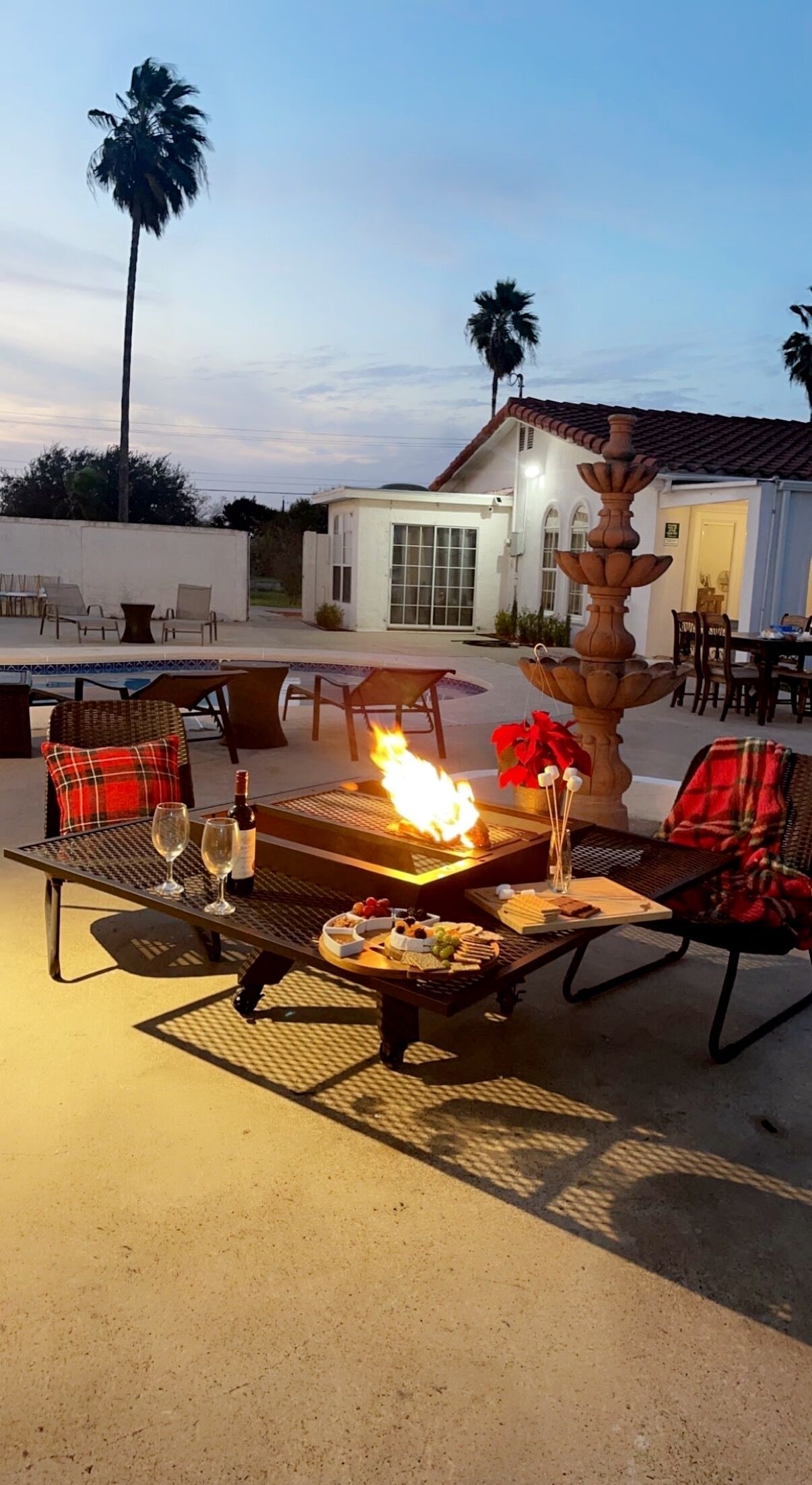 Un patio al aire libre con un hogar para fuego, asientos y una mesa de comedor preparada para una comida.