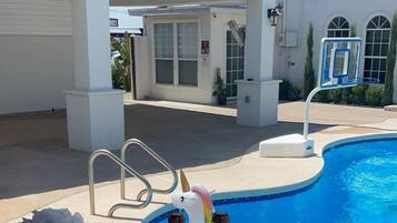 A poolside setting with a white building, a pool, and a unicorn float. There are bottles of Florentina sparkling wine, a glass pitcher, and a plate of oranges.