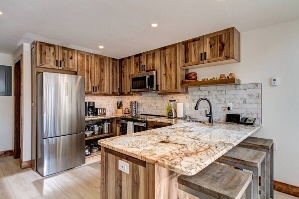 Une cuisine moderne avec des meubles en bois, des appareils électroménagers en acier inoxydable et un plan de travail en marbre.