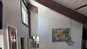 A hallway with a wooden door, a white wall, a painting, and a hanging light fixture.