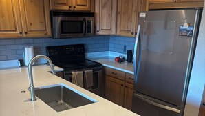 A kitchen with wooden cabinets, a stainless steel refrigerator, a microwave, and a sink.