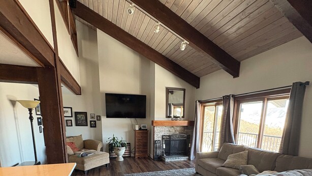 A spacious living area with a high ceiling, wooden beams, a fireplace, a sofa, a TV, and a dining area with a table and chairs.