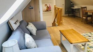 Een modern loft appartement met een grijze bank, een houten eettafel en een trap.