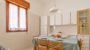 Eine Küche mit Esstisch für vier Personen, Holzstühle, einem Fenster mit Vorhängen und weißen Schränken.