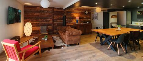 Una sala de estar moderna con una pared de madera, un sofá, una mesita de centro y un comedor con sillas.