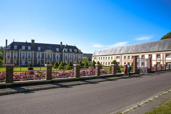 A large, historic building with a symmetrical facade, a central entrance, and a well-maintained garden with pink flowers and trimmed hedges. - The Philippines (Criel-sur-Mer)