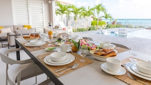 A breakfast table set with white plates, bowls, and cups, overlooking a pool and palm trees. - Eden Roc Villas (Le Diamant)