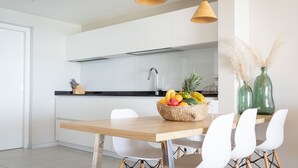 A modern kitchen with white cabinets, a wooden dining table, and a fruit basket. - Eden Roc Villas (Le Diamant)
