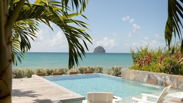 A wooden deck with a pool, lounge chairs, and a view of the ocean. - Eden Roc Villas (Le Diamant)