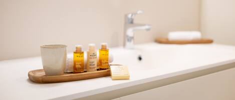 A bathroom counter with a white sink, a wooden tray holding a ceramic mug and three Nuxe skincare bottles, and a soap bar.
