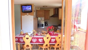 A dining area with a table set for four, wooden chairs, and a television mounted on the wall. - Spacious chalet 10 ppl, southeast, pets allowed (Valloire)