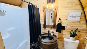 A cozy, wooden cabin bathroom with a bathtub, toilet, and a wooden barrel sink.