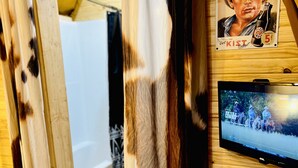 A room with a wooden interior, a mounted television displaying a movie, a potted plant, and a curtain with a spotted pattern.