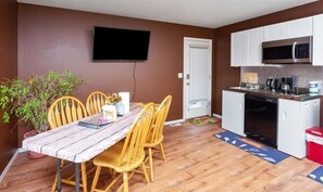 Un espace de vie compact comprenant un coin repas, une kitchenette et un téléviseur à écran plat fixé au mur.