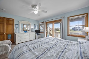 A bedroom with a bed, dresser, television, and a view of the outside.